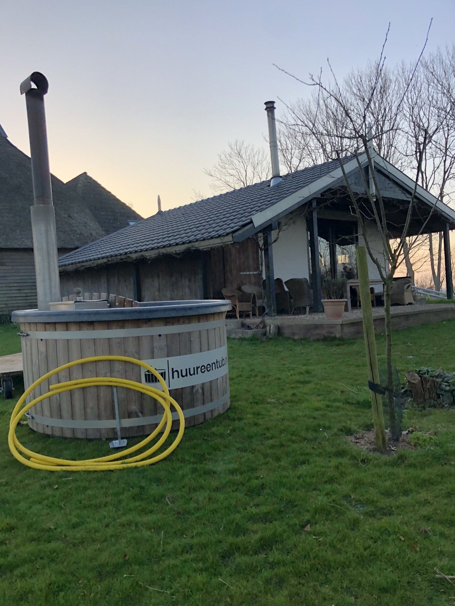 Een houten hot tub staat in het gras voor een vakantie huis. 