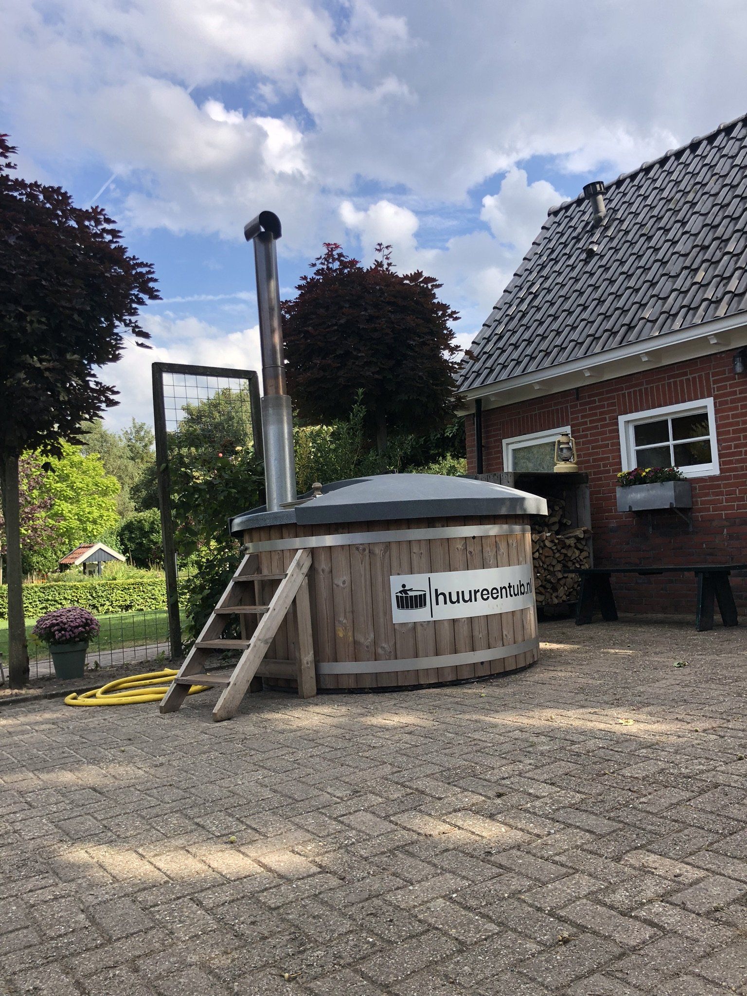 Een houten hottub staat voor een bakstenen huis.