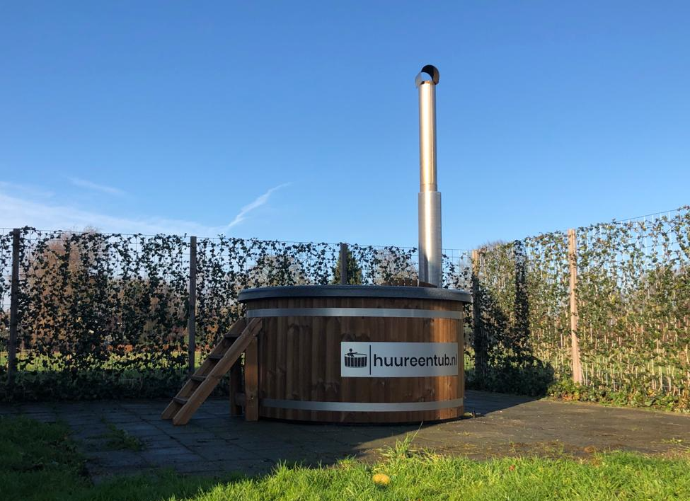Een houten hottub staat midden in een grasveld.