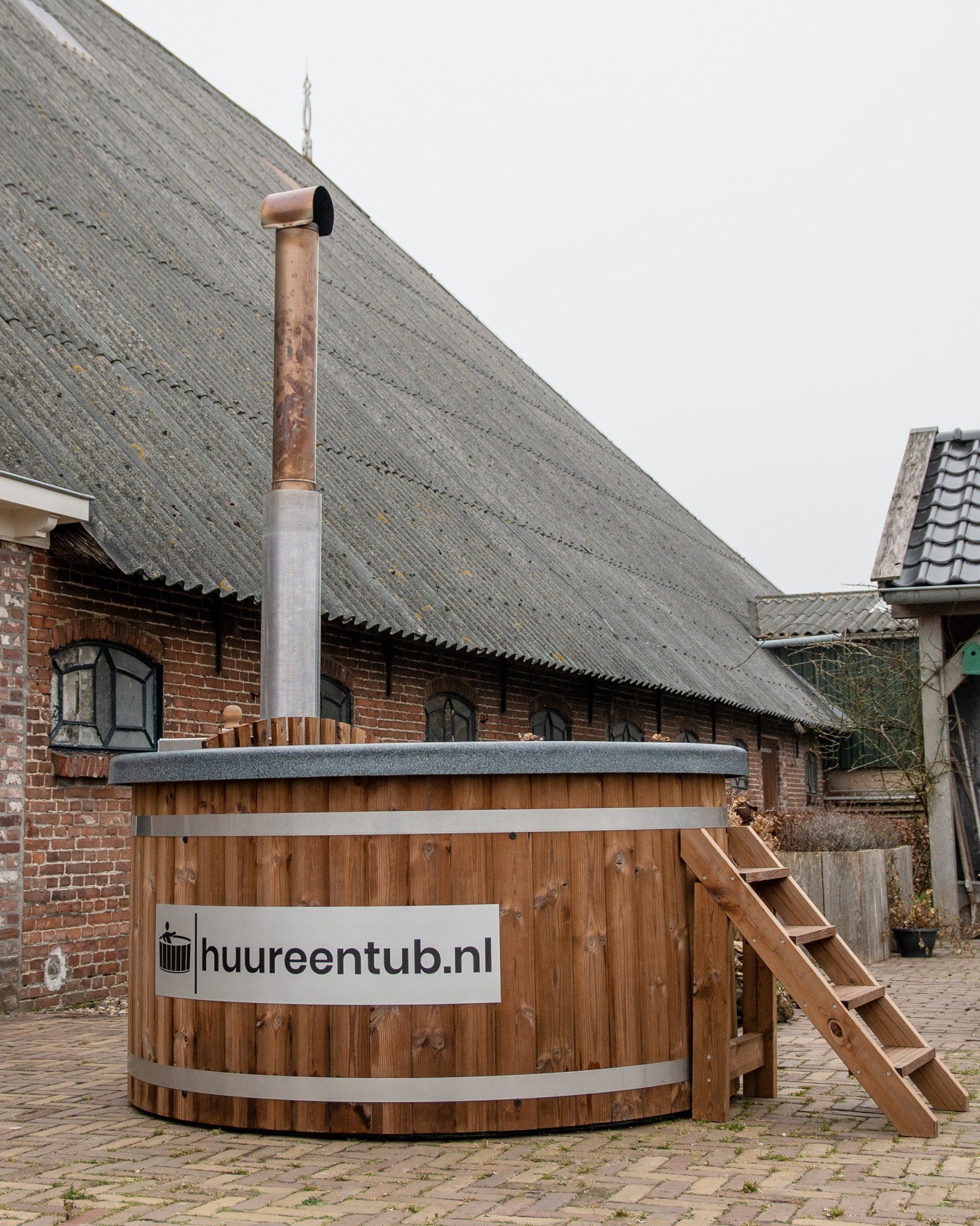 Een houten hottub staat voor een bakstenen gebouw.