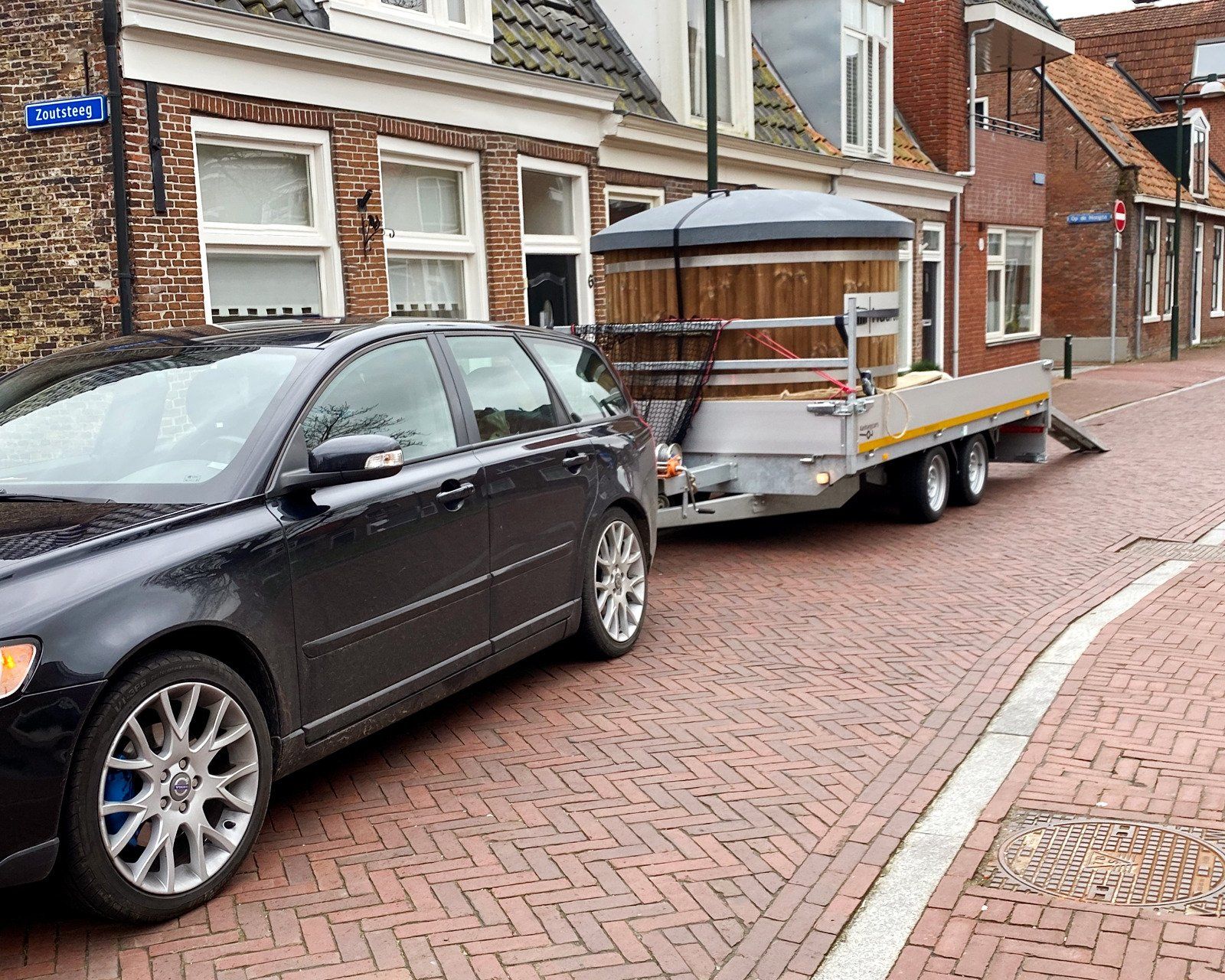 Een zwarte auto staat geparkeerd voor een aanhanger met een hot tub erop.