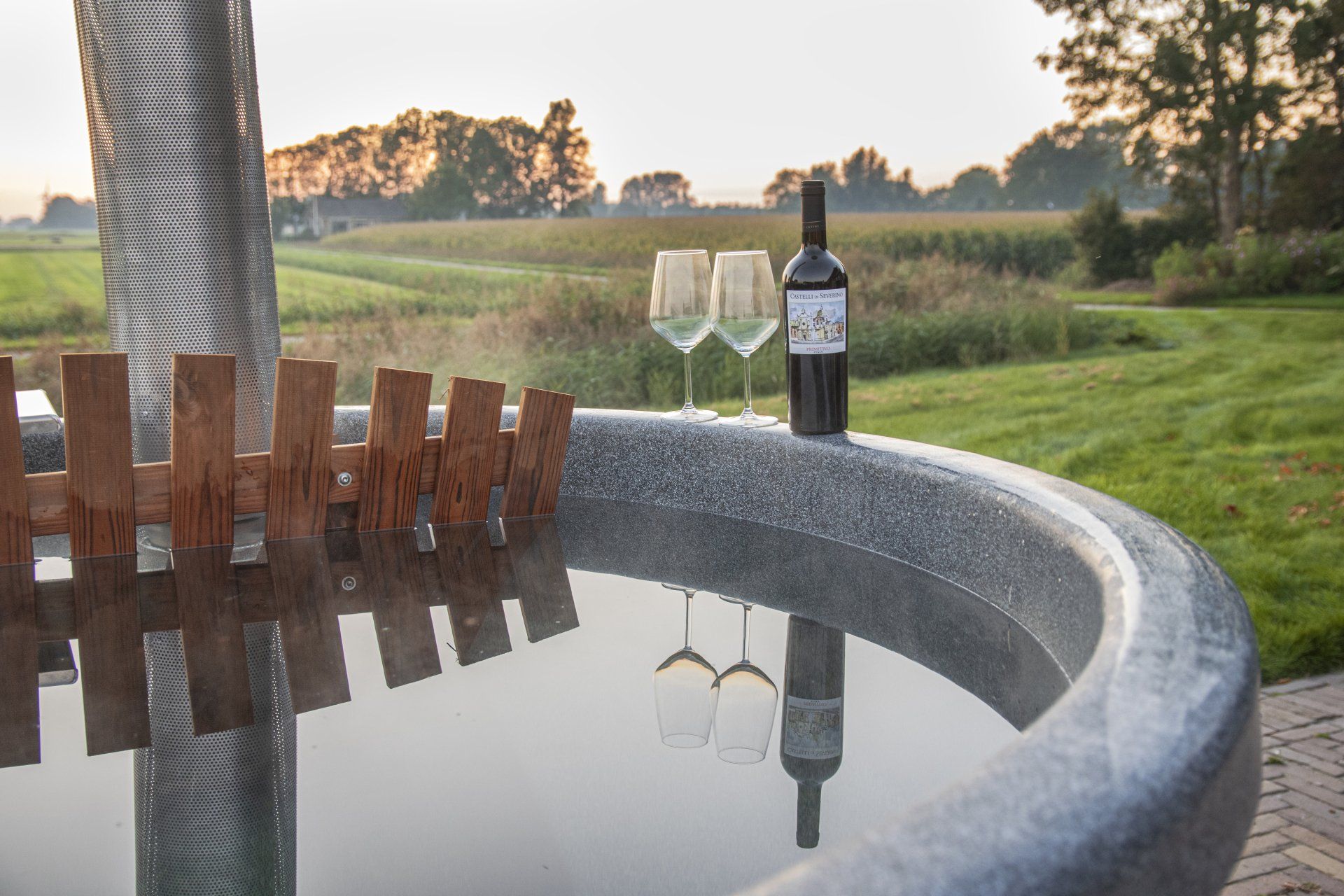 Een fles wijn en twee wijnglazen staan bij een hot tub.