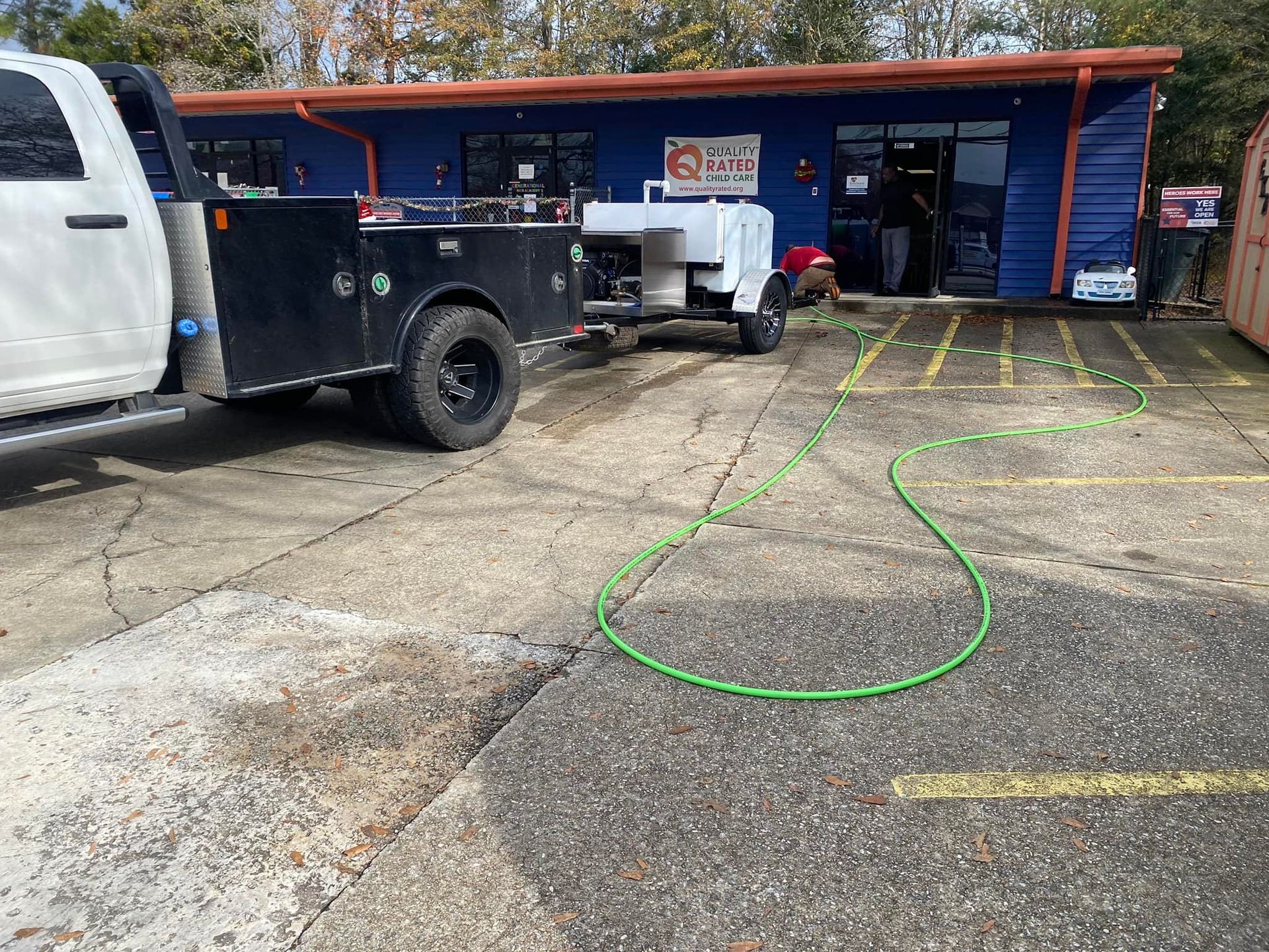 A white truck is parked in front of a building with a green hose attached to it.