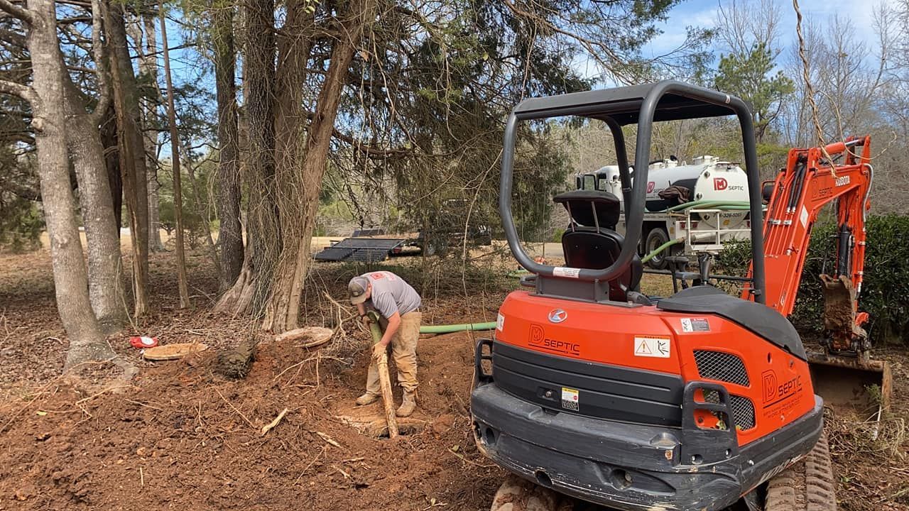 A man is digging in the dirt next to a small excavator.