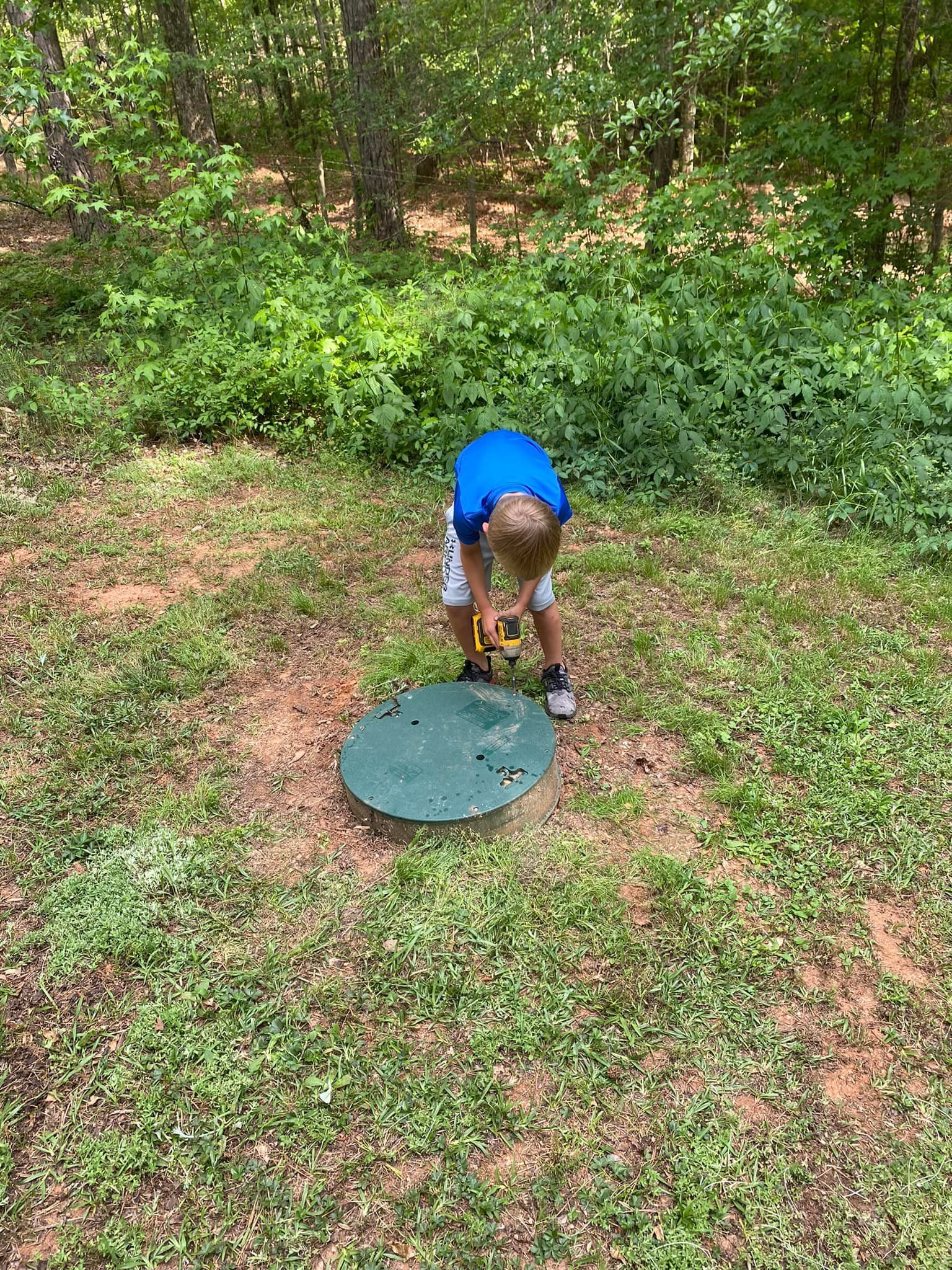 A young boy is working on a septic tank in the grass.