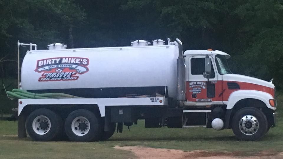 A white and red dirty mike 's septic truck is parked in a grassy field.