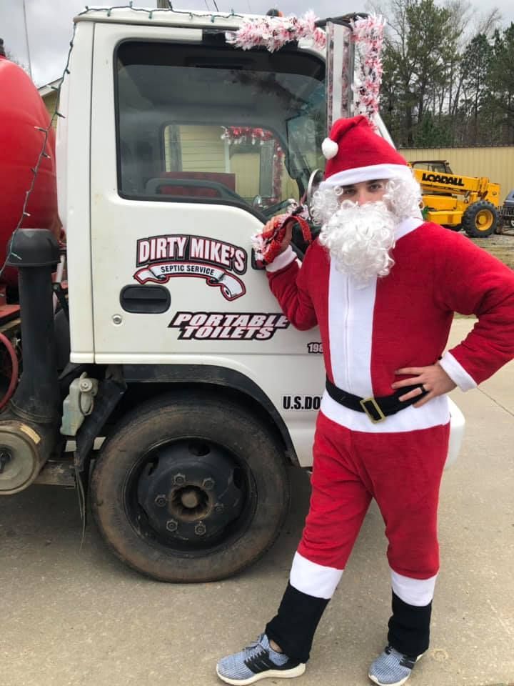 A man dressed as santa claus is standing in front of a dirty mikes truck