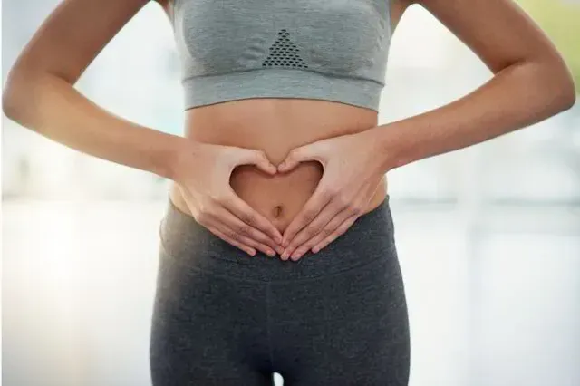 Person in a gray sports bra and dark leggings forming a heart shape with their hands over their stomach