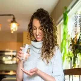 Woman in a cozy kitchen examining a glass in her hand, smiling under warm pendant lights