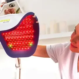 Person using a red LED facial therapy mask in a bright clinic setting