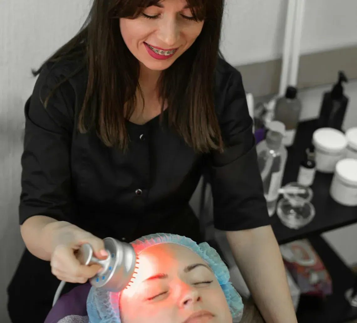 Facial treatment with glowing device on client, spa technician in black working beside treatment bed