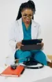 Healthcare worker in teal scrubs with headset, speaking at a desk with laptop and stethoscope