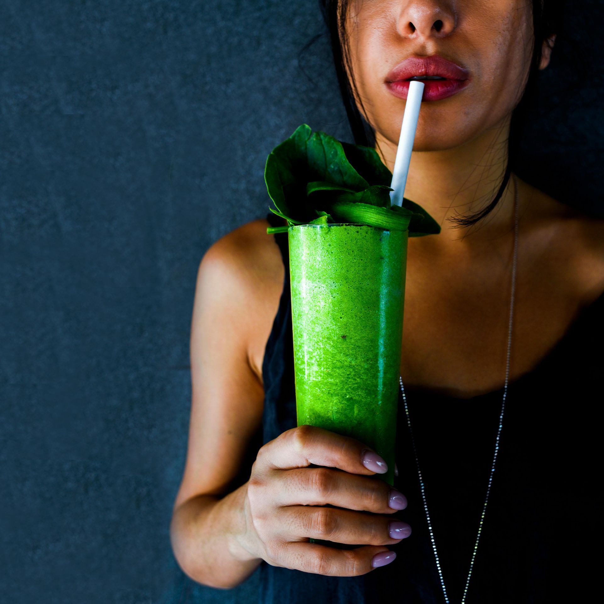 Person holding a bright green smoothie with mint and a straw against a dark background