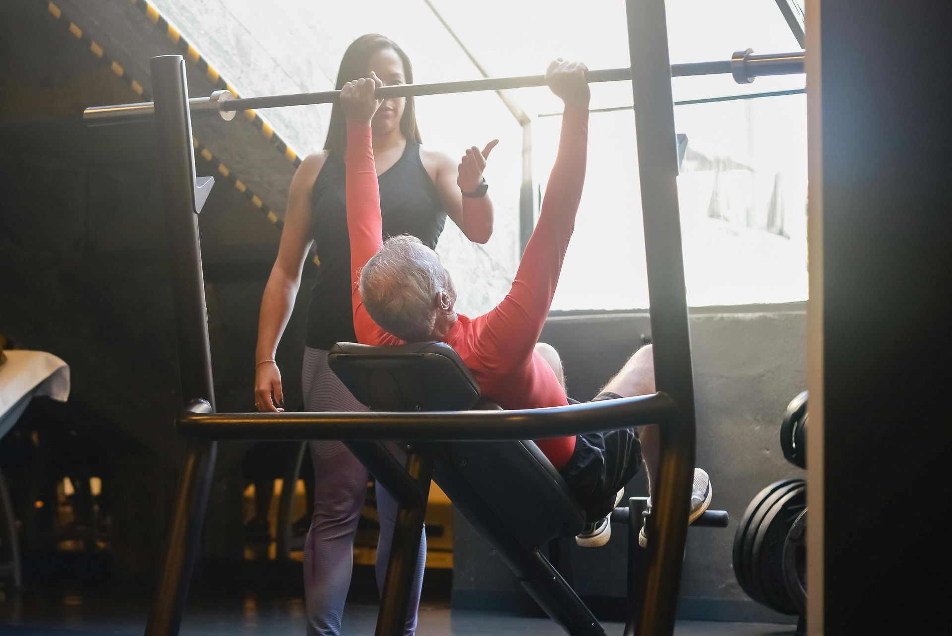 Gym training session with a coach spotting a person doing a seated pull-up on a machine