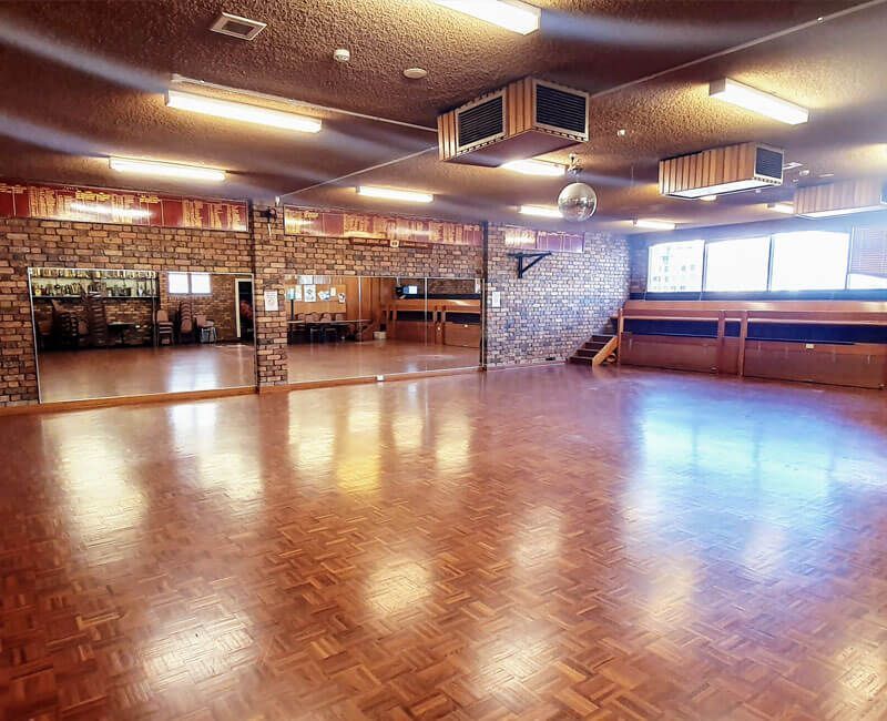 Empty dance studio with wooden floor, mirrored wall, exposed brick, and disco ball.