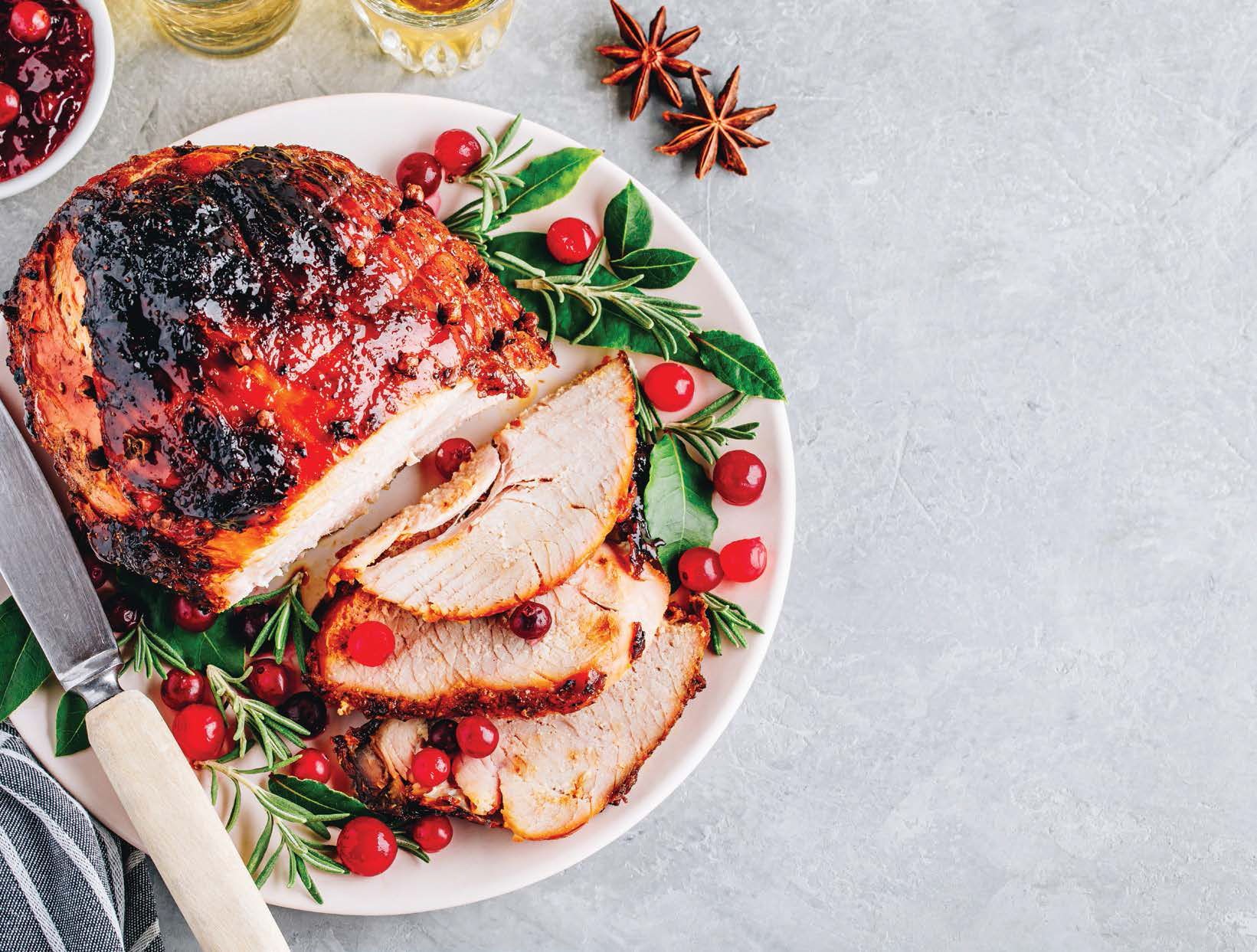 Roasted ham with cranberry garnish on a plate, side of sauce, festive presentation.