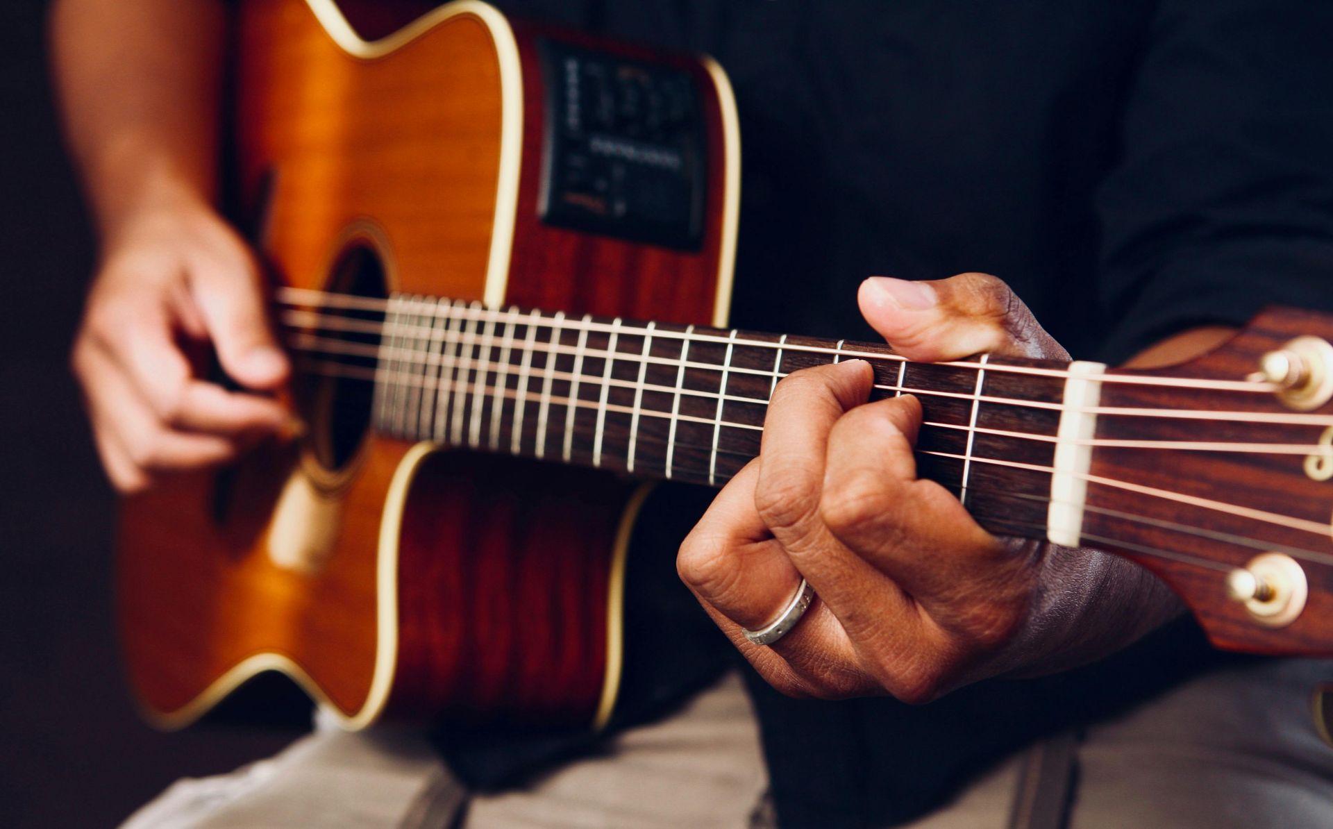 Person's hands playing an acoustic guitar. Brown guitar, fingers on frets, strumming.