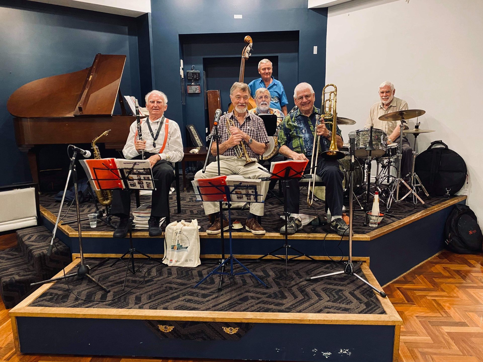Jazz band performing on a small stage. Musicians play instruments, including saxophone, trumpet, drums, piano, and bass.