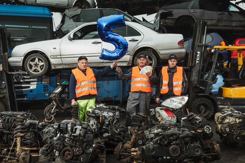 Trys vyrai, stovintys prieš krūvą automobilių detalių