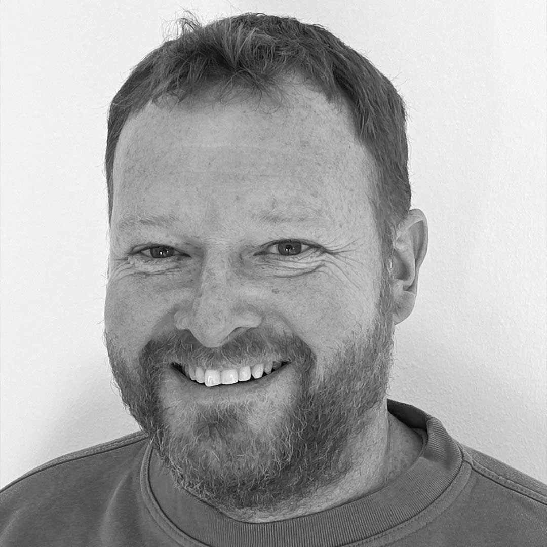 Jens har skæg smiler på et sort/hvidt foto.