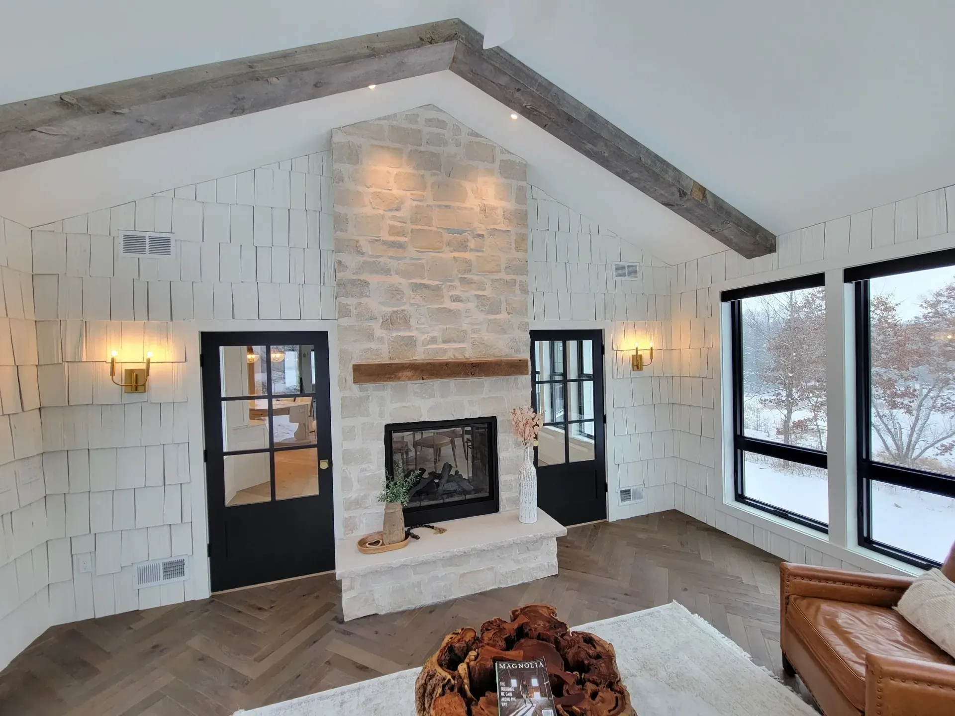 Bright modern living room with white walls, stone fireplace, wood floor, and large windows