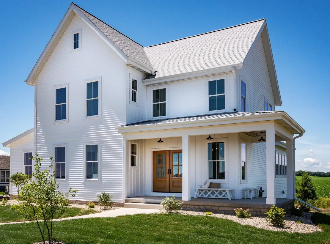 White two-story house with wraparound porch and peaked roof on a sunny day
