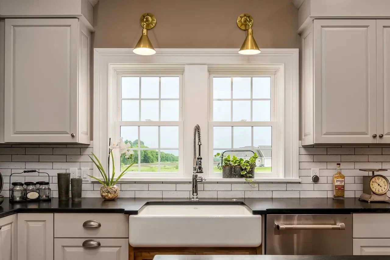Bright modern kitchen with white cabinets, farmhouse sink, and two windows above the counter.