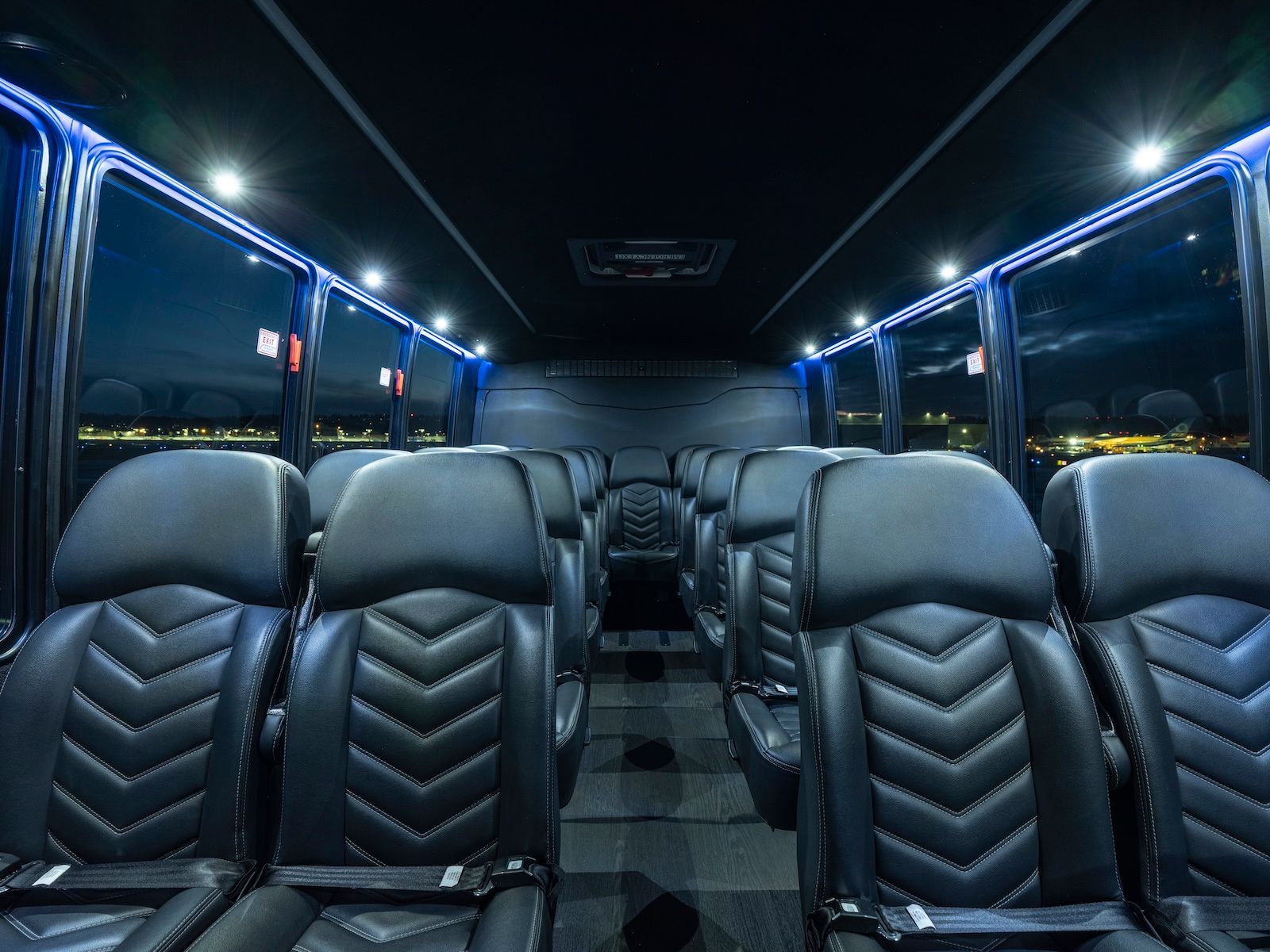 Interior of a luxury passenger vehicle with rows of black quilted leather seats and ambient blue LED ceiling lighting.