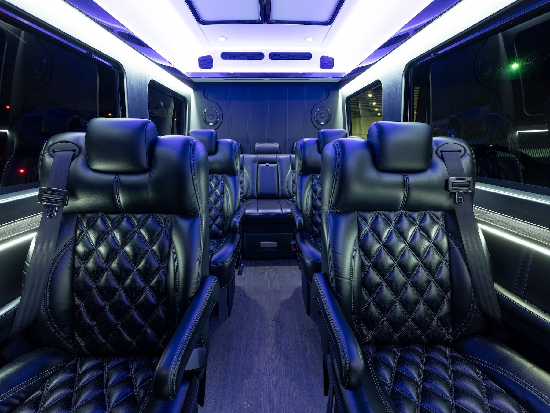 Interior view of a luxury shuttle bus featuring rows of black quilted leather captain's chairs and ambient blue lighting.