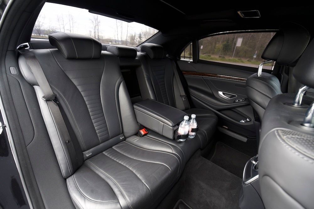 The interior of a vehicle featuring black leather bucket seats and a central console, viewed from the second row.