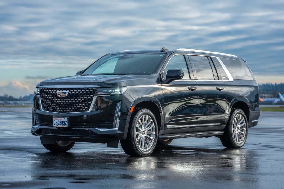 A black Cadillac Escalade SUV parked on a wet, paved surface against a cloudy sky.
