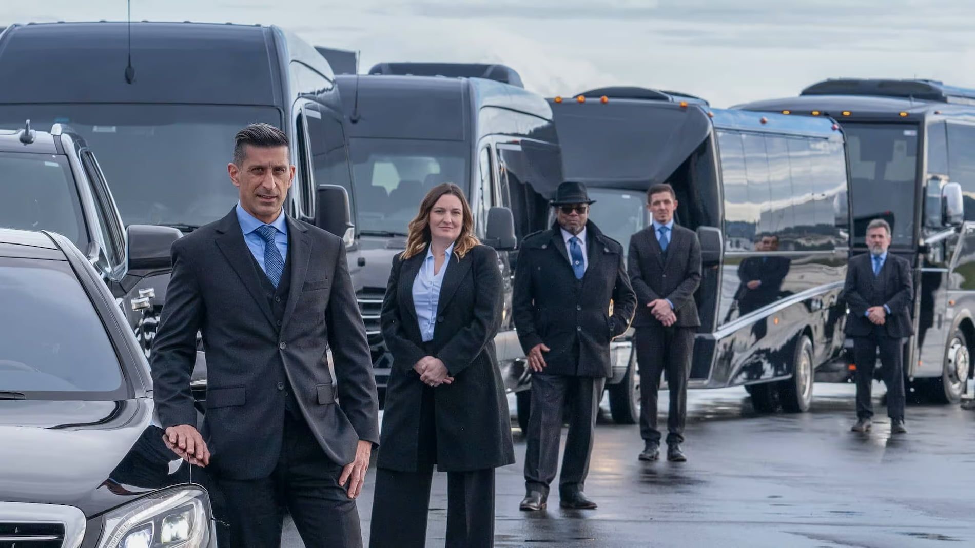 Professional group standing in front of a line of luxury black vehicles parked outdoors on a paved lot.