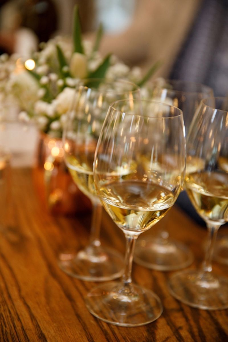 Several glasses of white wine arranged on a wooden table with a soft-focus flower arrangement in the background.
