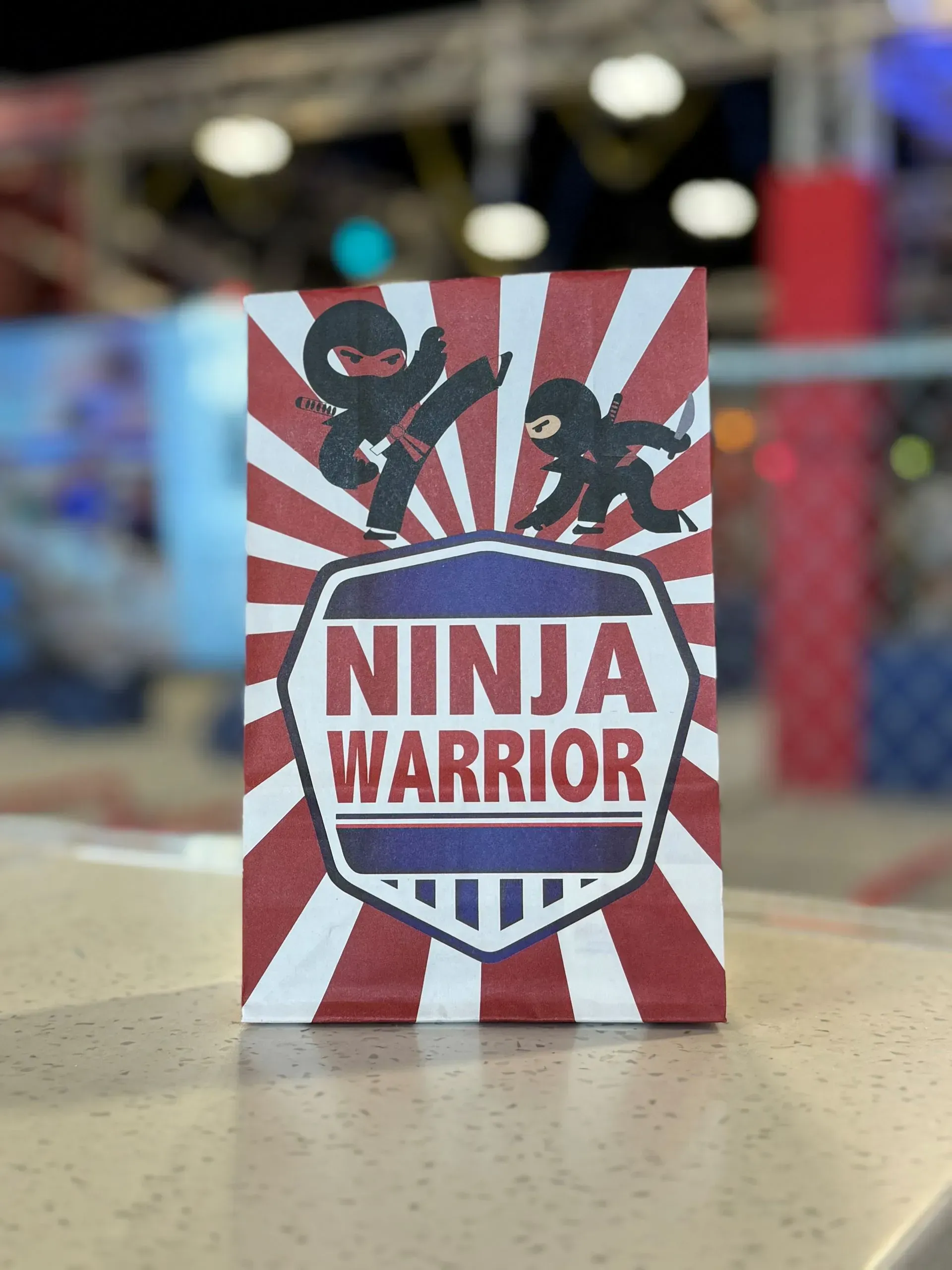 Ninja Warrior sign with ninja figures on a red, white, and blue background.