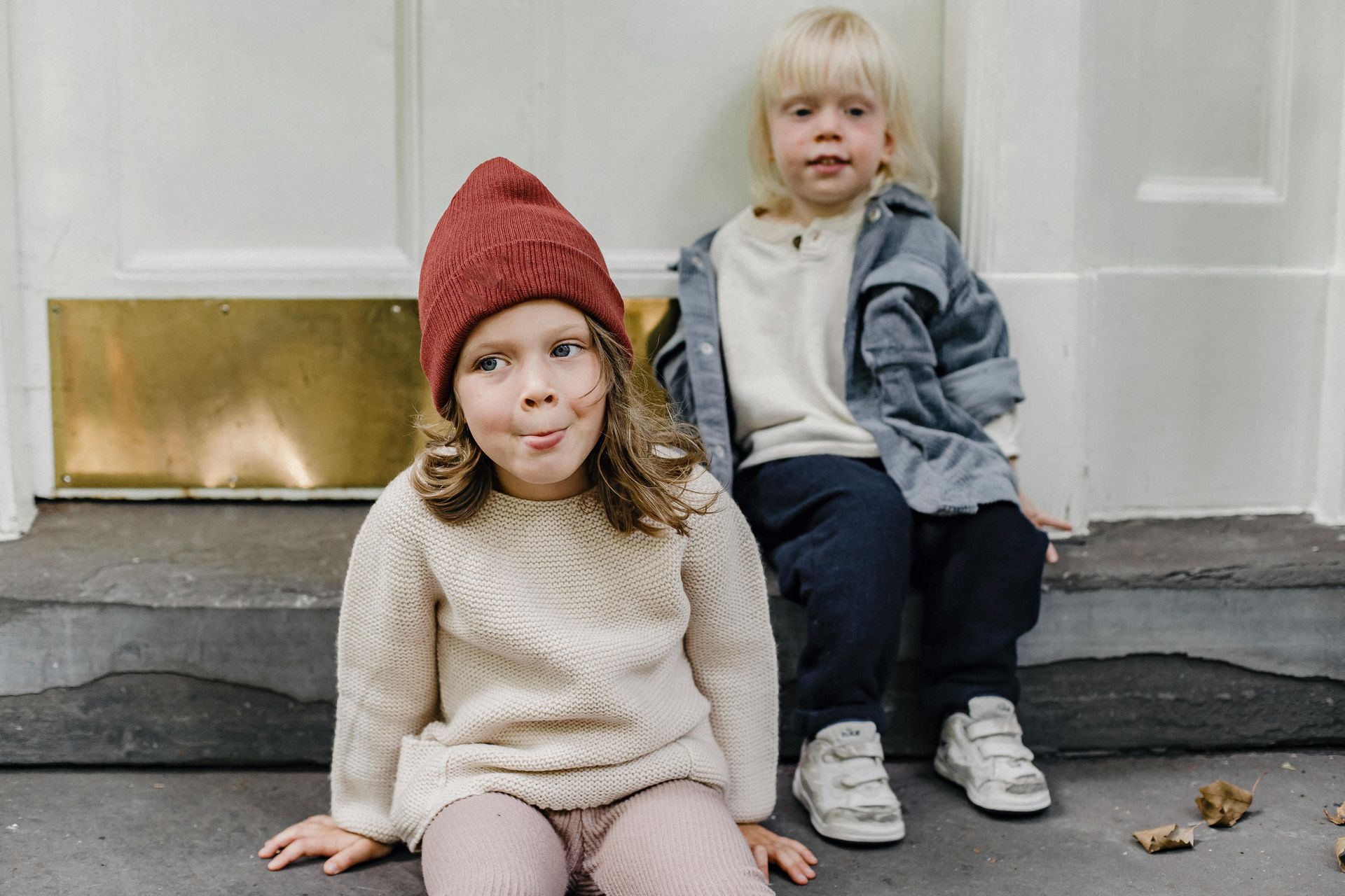Two children sitting on steps; one sticking out their tongue, the other looking on.