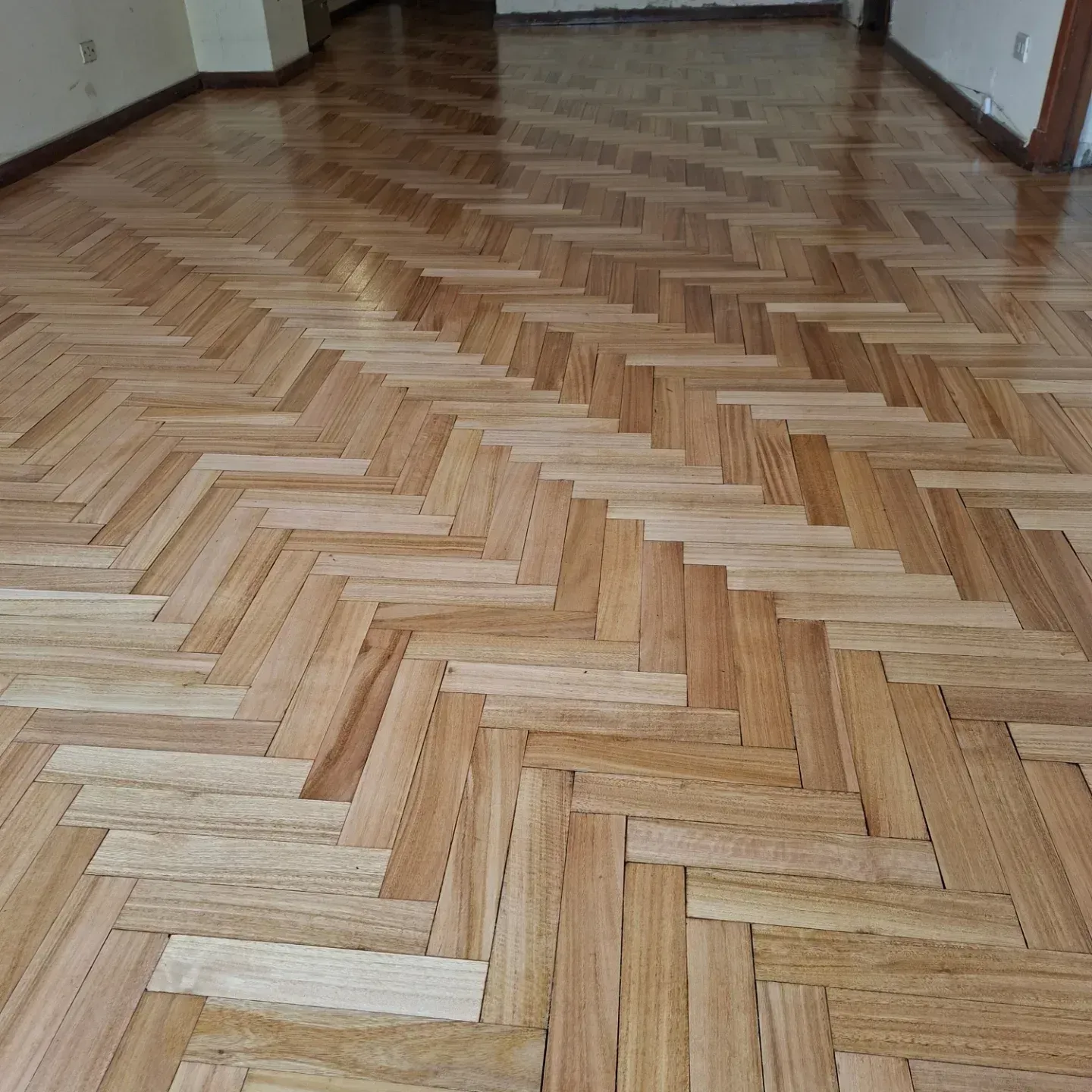 Habitación vacía con suelo de madera en espiga y paredes desnudas.
