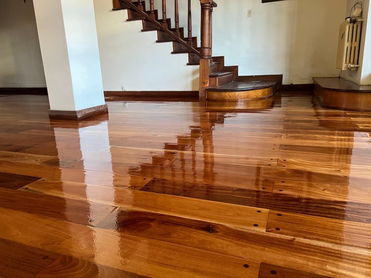 Suelo de madera pulida que refleja una escalera en una habitación luminosa y vacía.