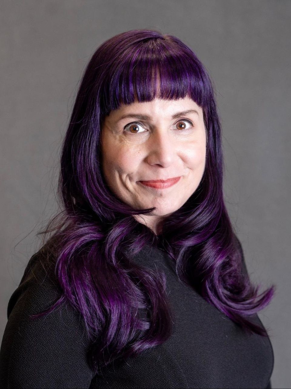 a woman with purple hair and a black shirt is smiling for the camera .