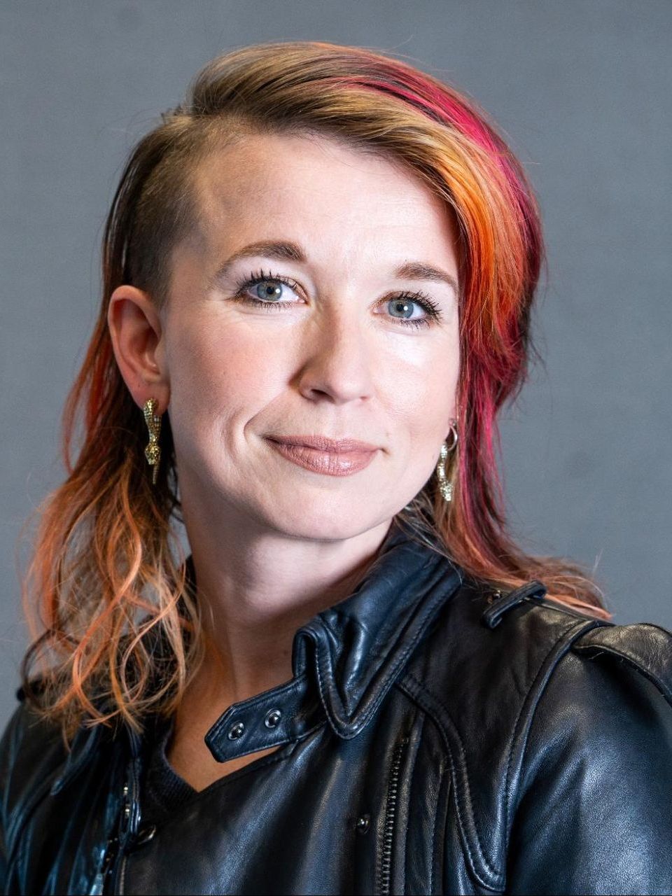 a woman with red hair is wearing a black leather jacket and earrings .