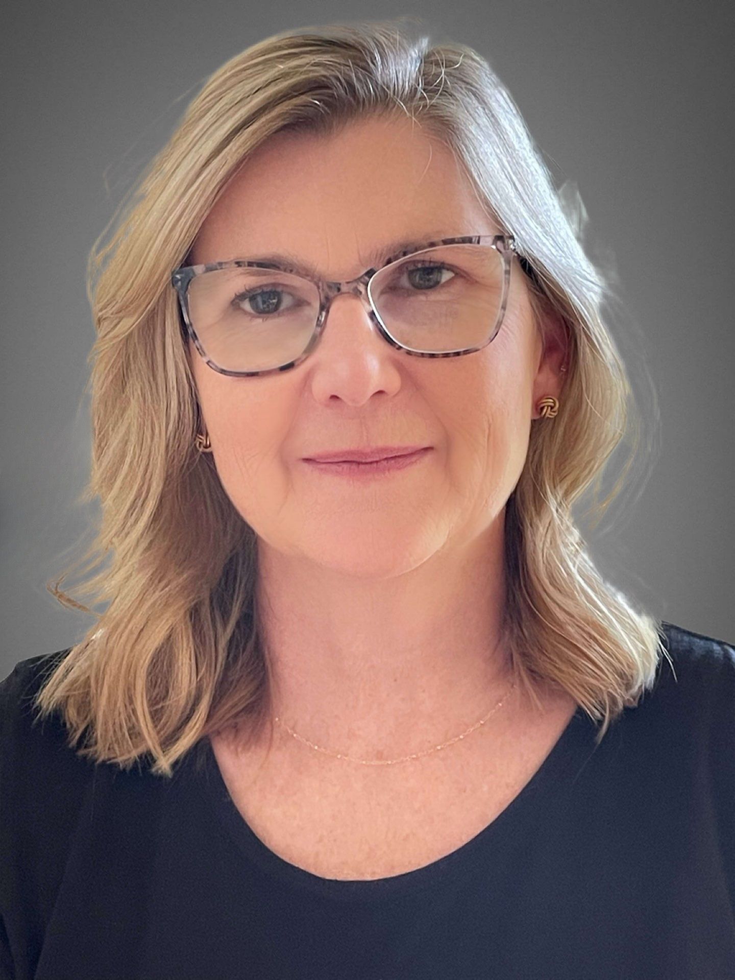 a woman wearing a purple shirt and a green necklace is smiling for the camera .