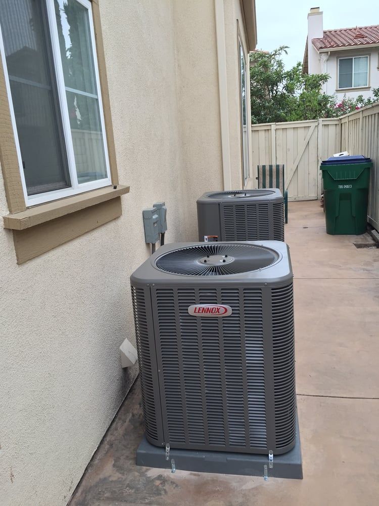 Two air conditioners are sitting outside of a house next to a window.