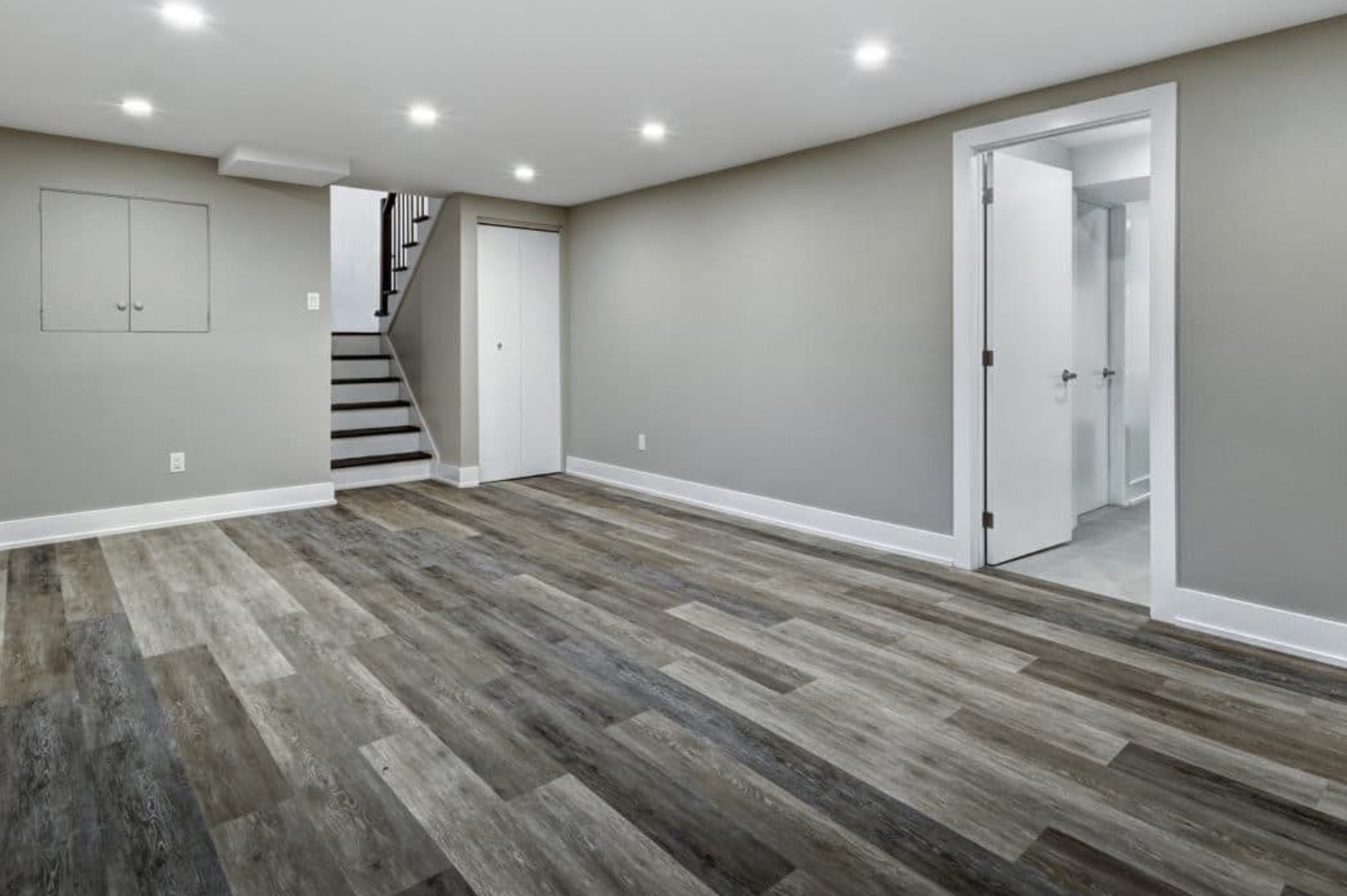 An empty basement with hardwood floors and stairs leading to a bathroom.