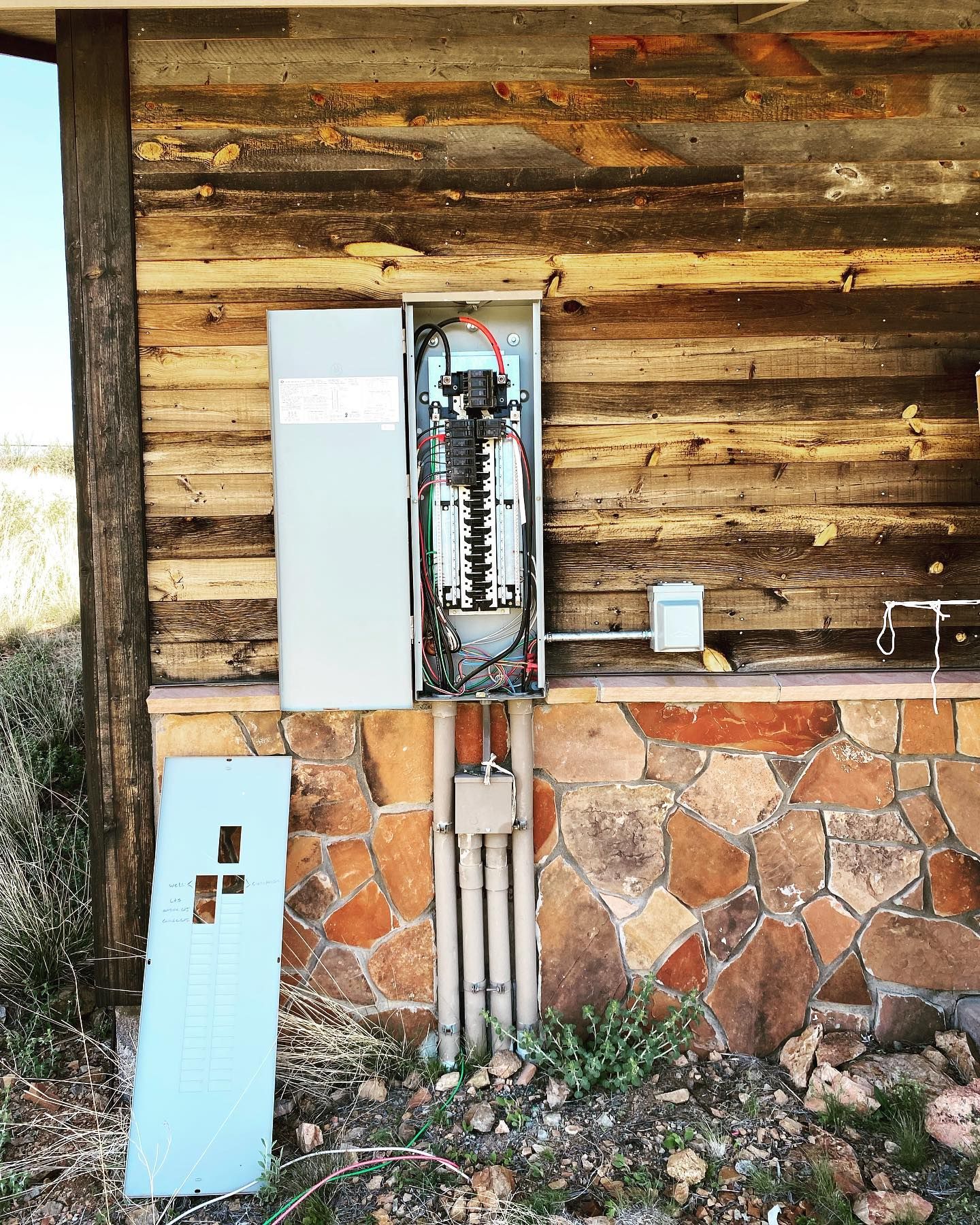 A electrical box is sitting on the side of a wooden building.