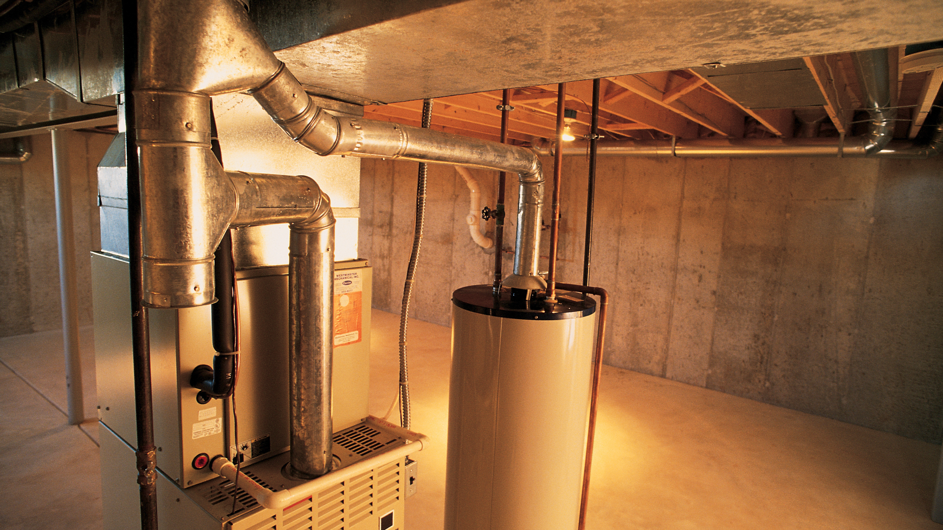 Furnace and water heater in a basement with silver ductwork, pipes, and concrete walls.