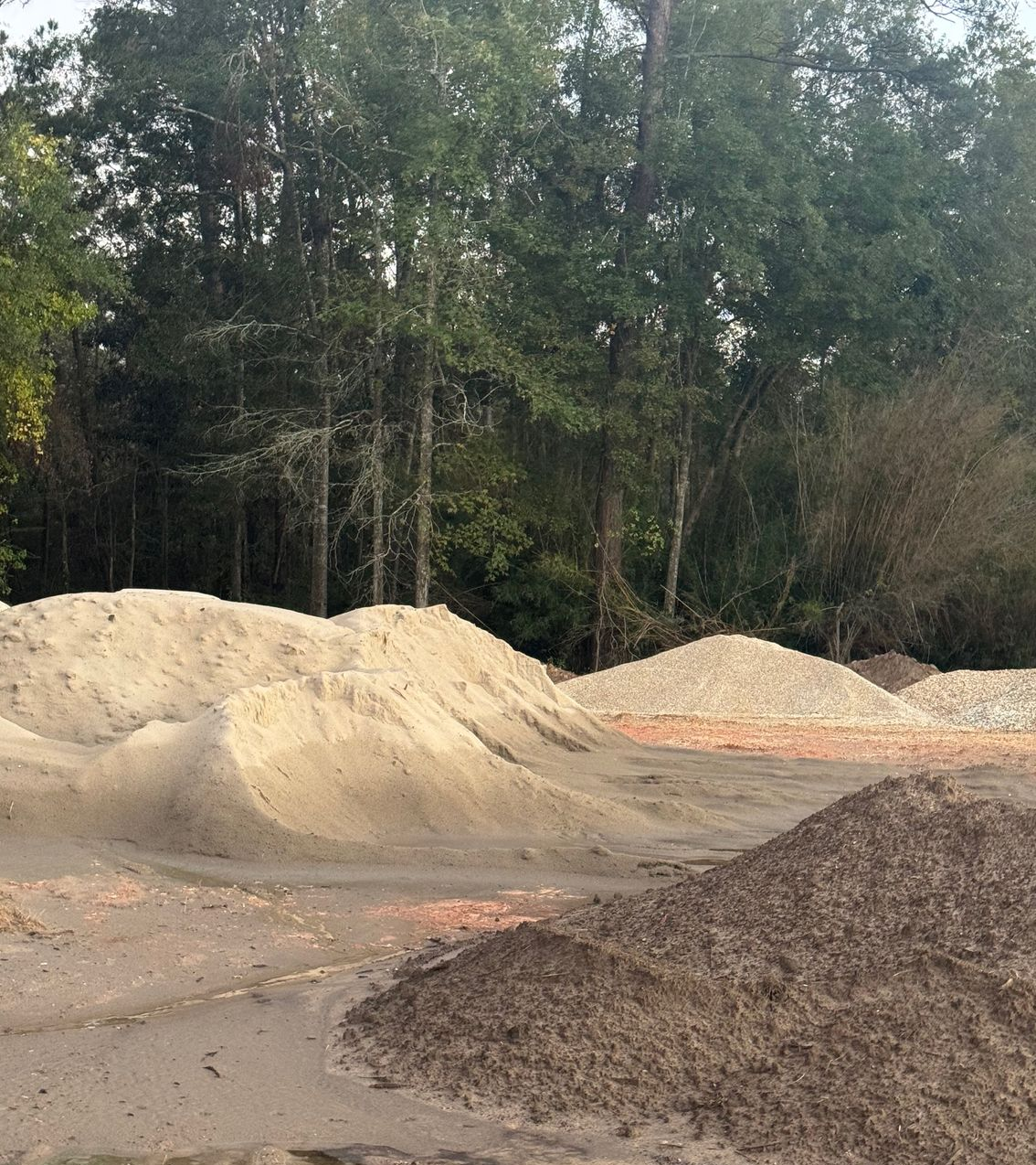 Piles of sand and gravel in a construction site with trees in the background.