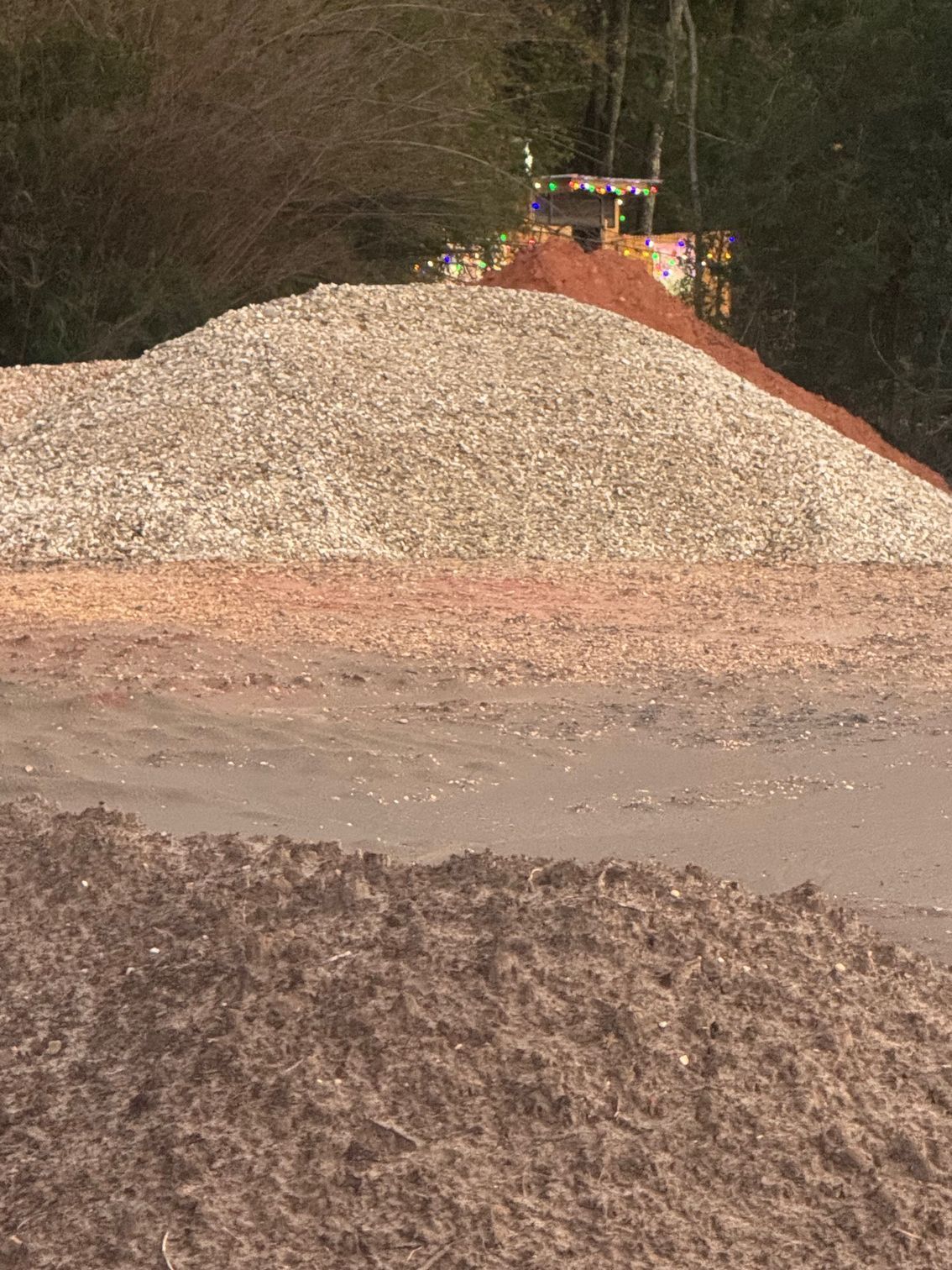 Piles of gravel and dirt in shades of brown and beige, with a backhoe visible in the background.