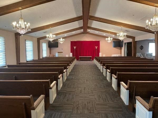 Funeral home interior with rows of wooden pews, red backdrop, and chandeliers.