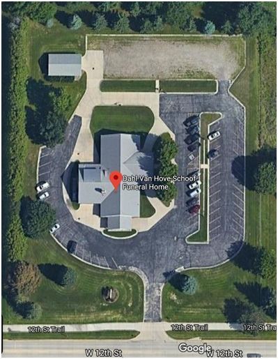 Aerial view of a building with a red location marker, surrounded by parking and green space.