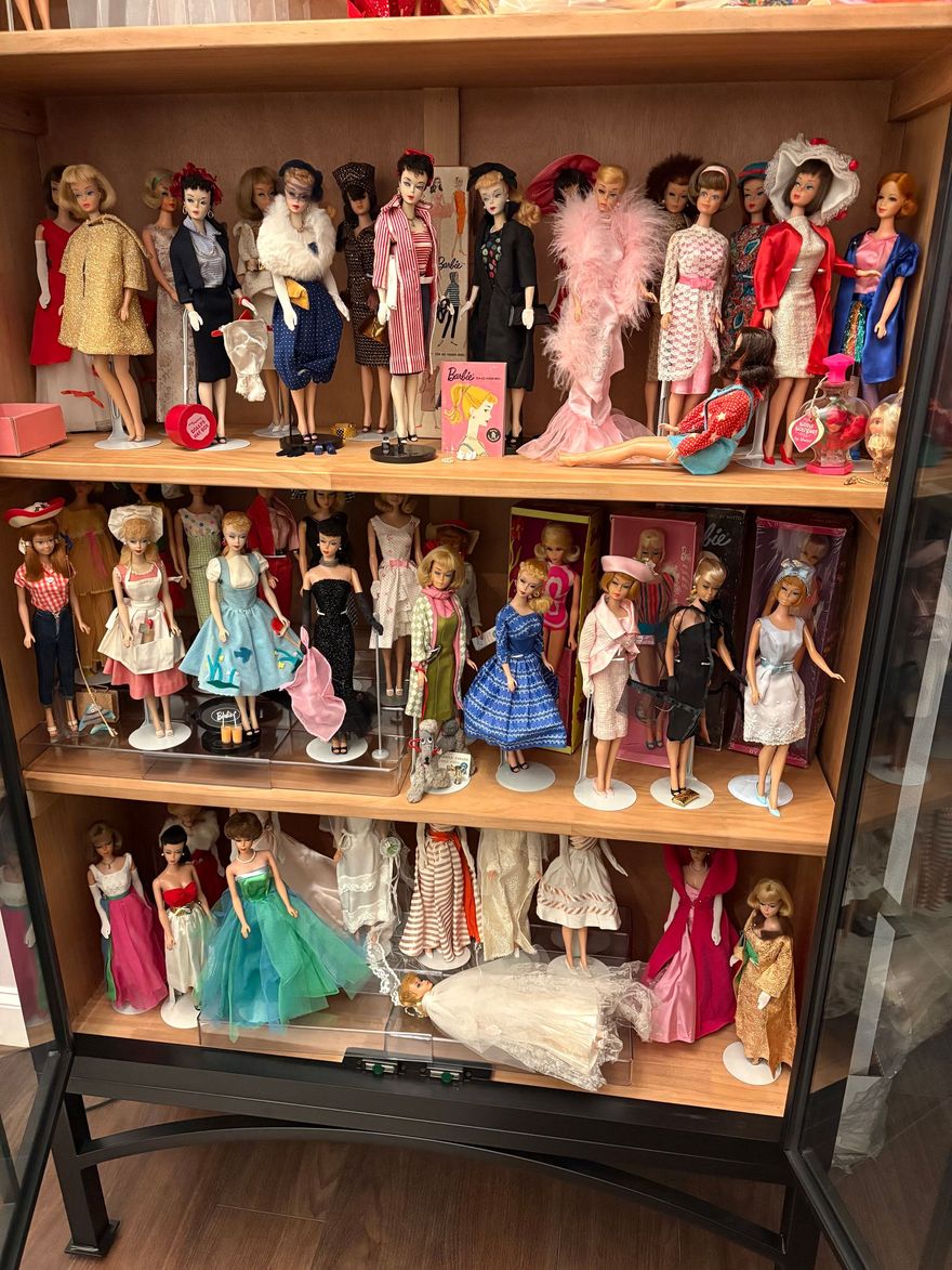 Shelves filled with colorful dolls in dresses and gowns on display in a wooden cabinet