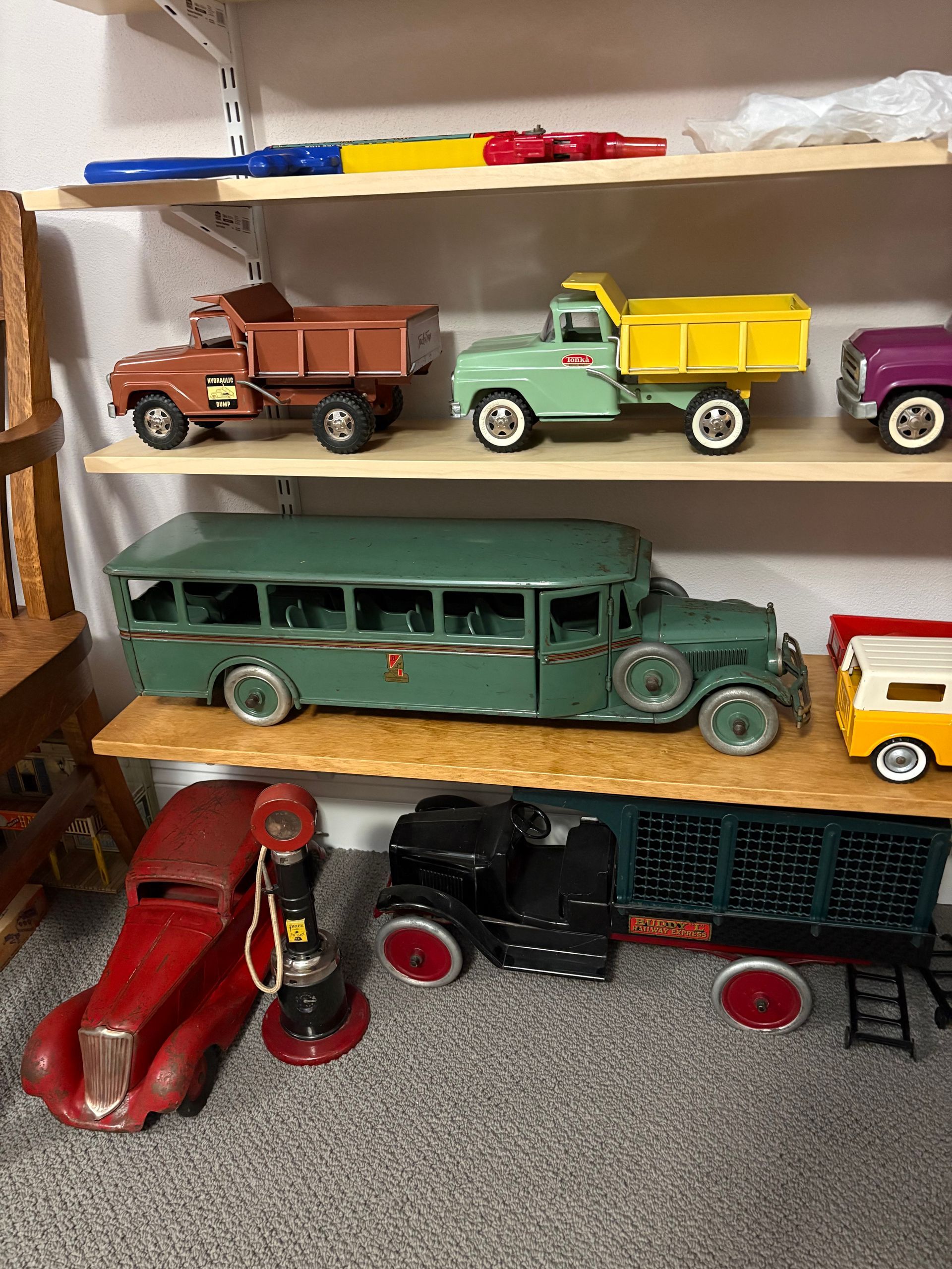 Shelves displaying assorted toy cars and trucks, including a long green vintage bus and red race cars.